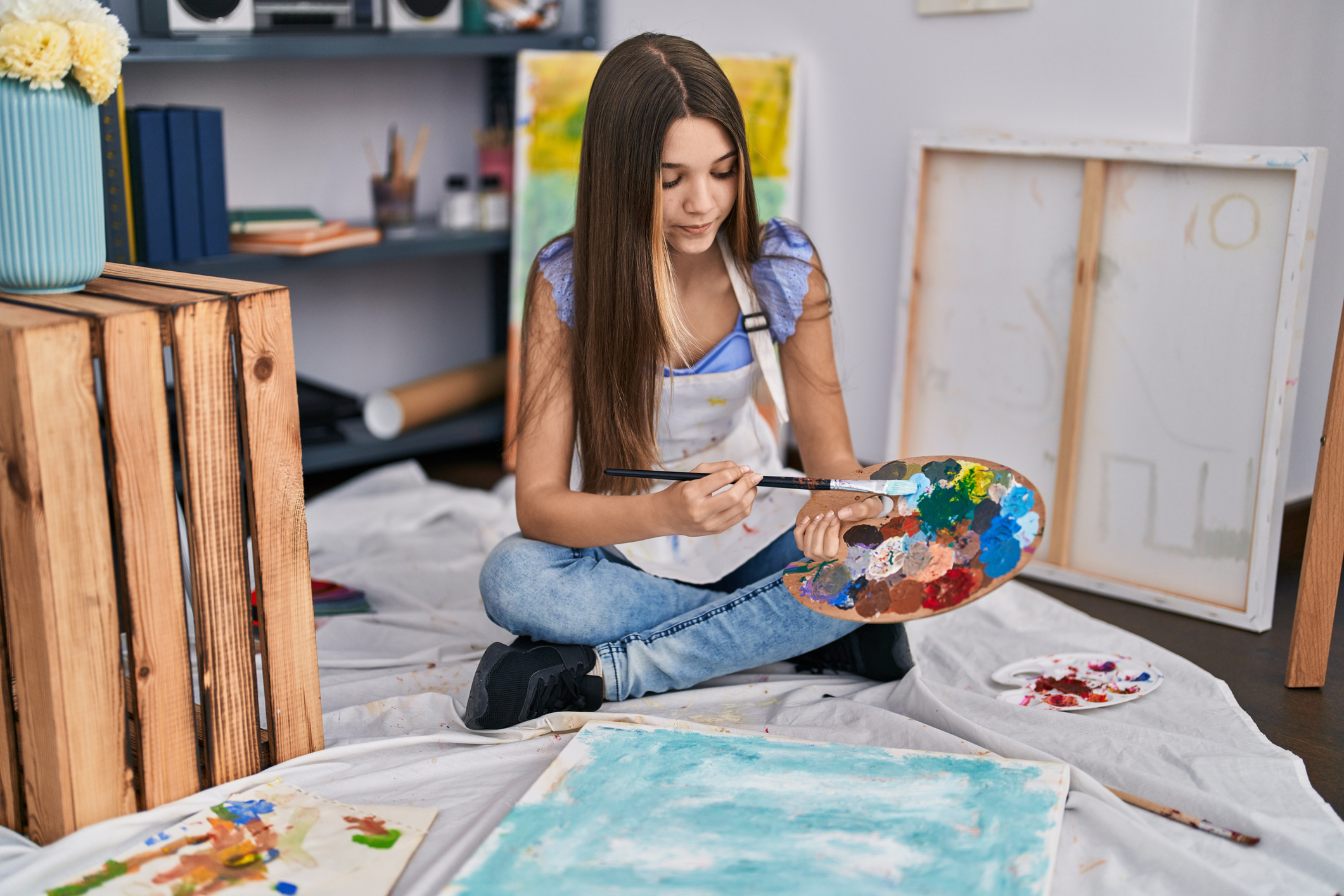 Adorable girl artist sitting on floor drawing at art studio